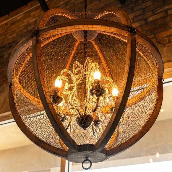 A rustic chandelier with a chicken wire and wood frame hangs in a brick-walled room.